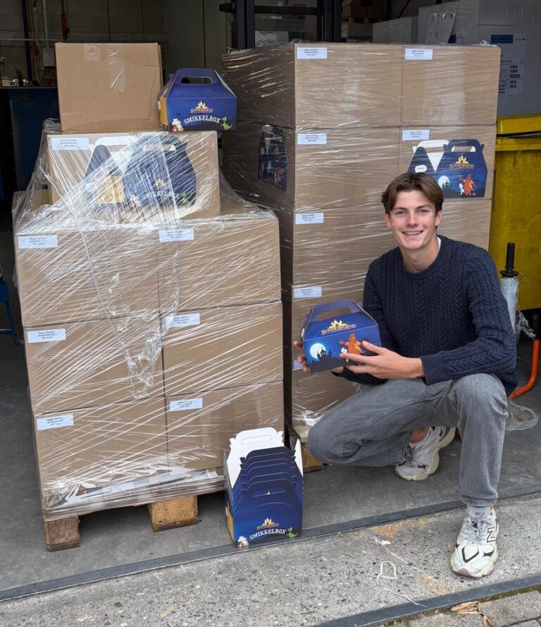 Persoon zittend met kidsbox in de hand, zittend naast een pallet vol kidsboxen